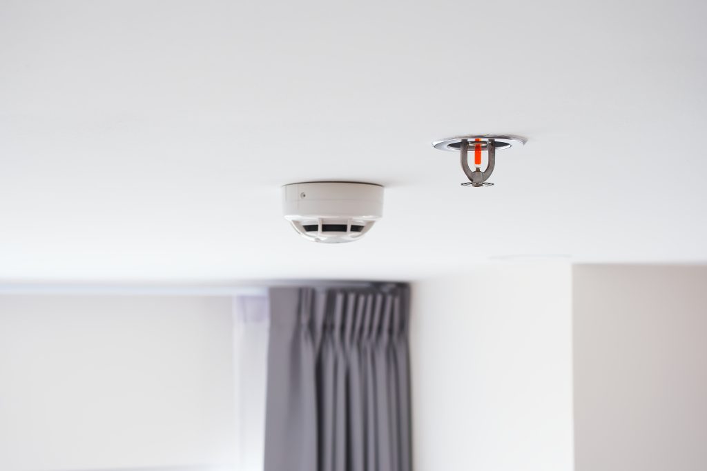 Ceiling-mounted smoke alarm and sprinkler system in a modern room, illustrating professional smoke alarm installation, replacement, and repair services in Melbourne.