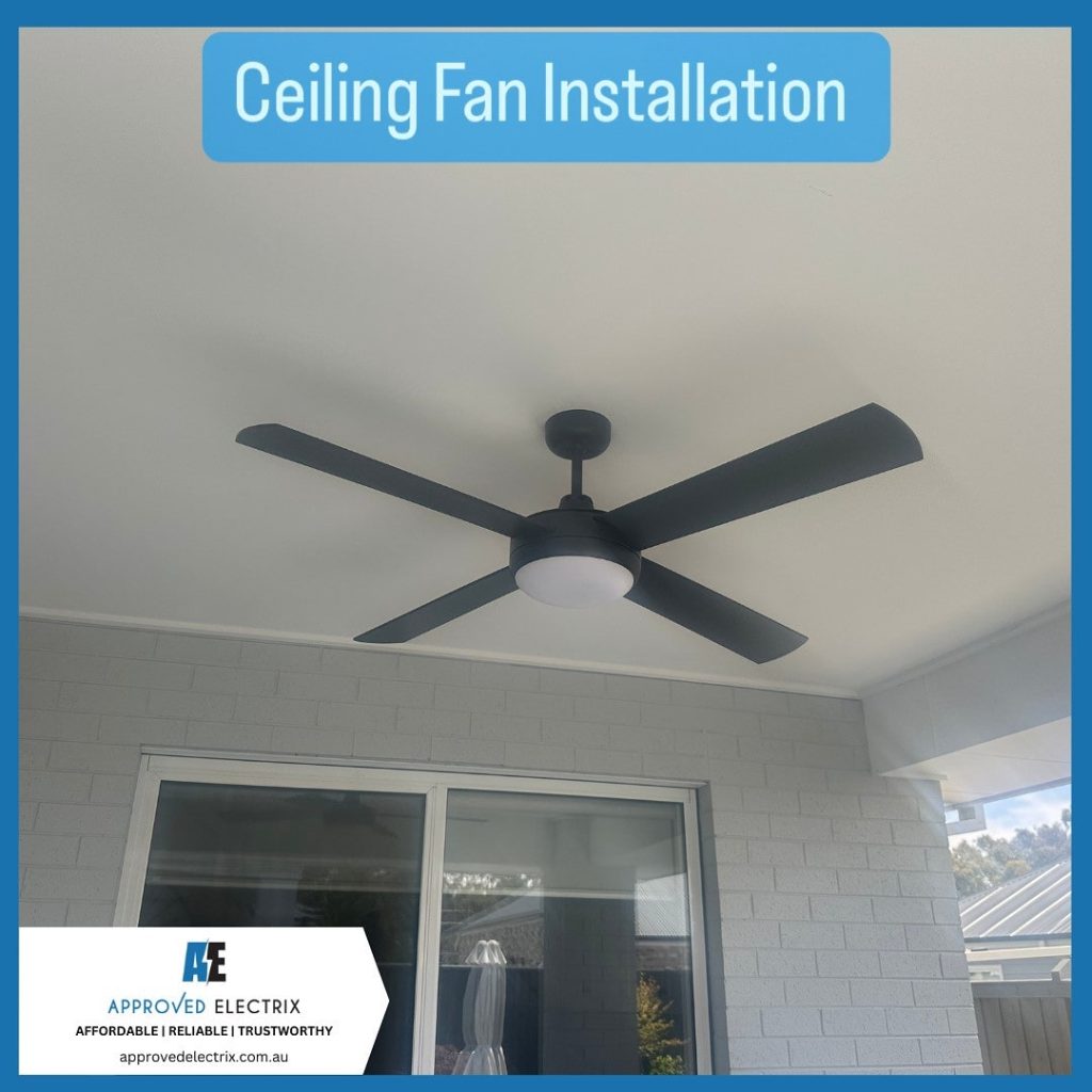 4 blade black ceiling with a light attached to the ceiling fan installed in a outdoor patio area with brick walls and a window in the background